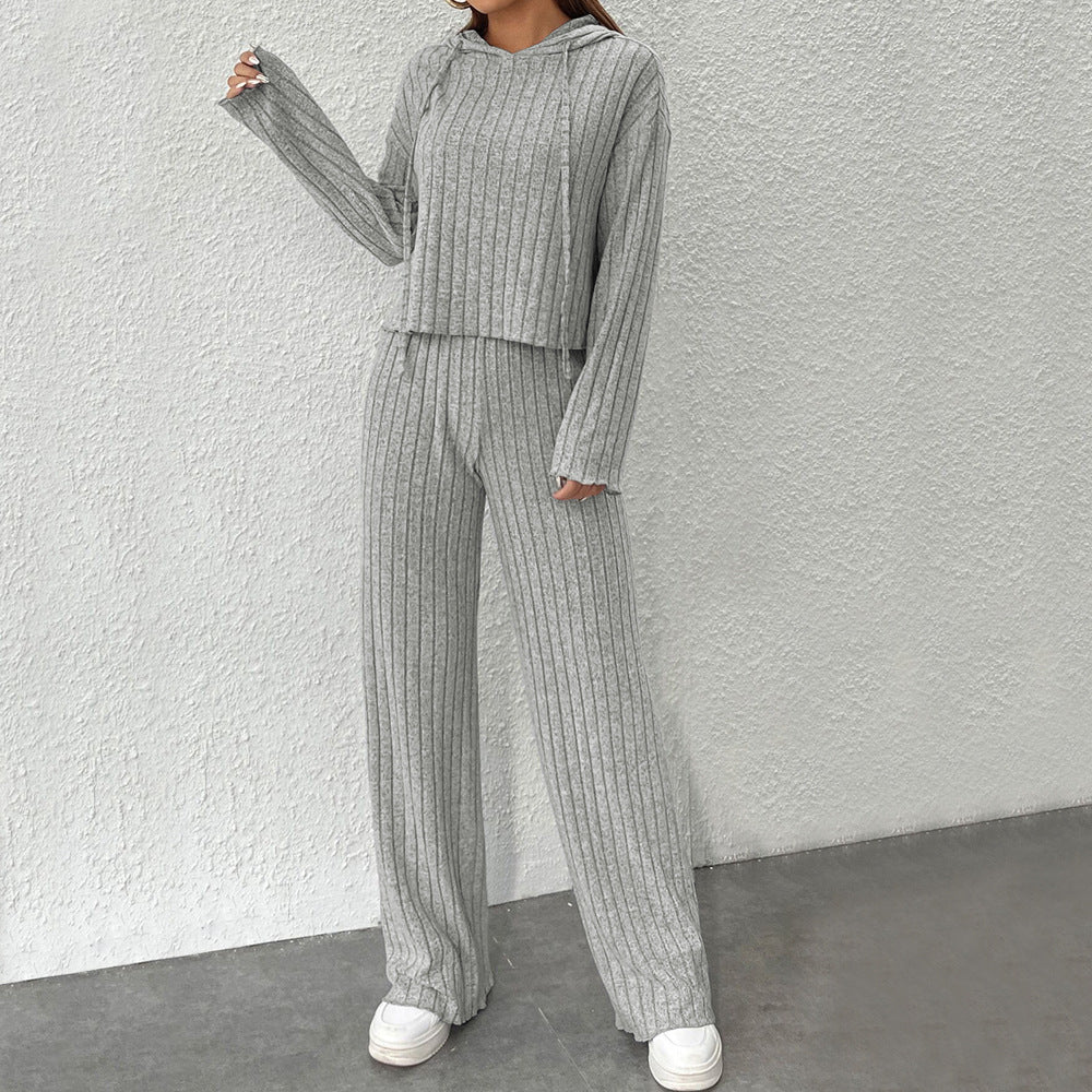 Frau in grauem, geripptem Strick-Set mit Kapuzenpullover und weiten Hosen, lässiger Look, modische Damenbekleidung, gemütlicher Stil.