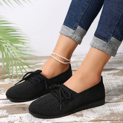 Damen tragen schwarze, gestrickte Sneakers mit Schnürsenkeln, kombiniert mit hochgekrempelten Jeans. Perfekt für Freizeitmode und Sommeroutfits.