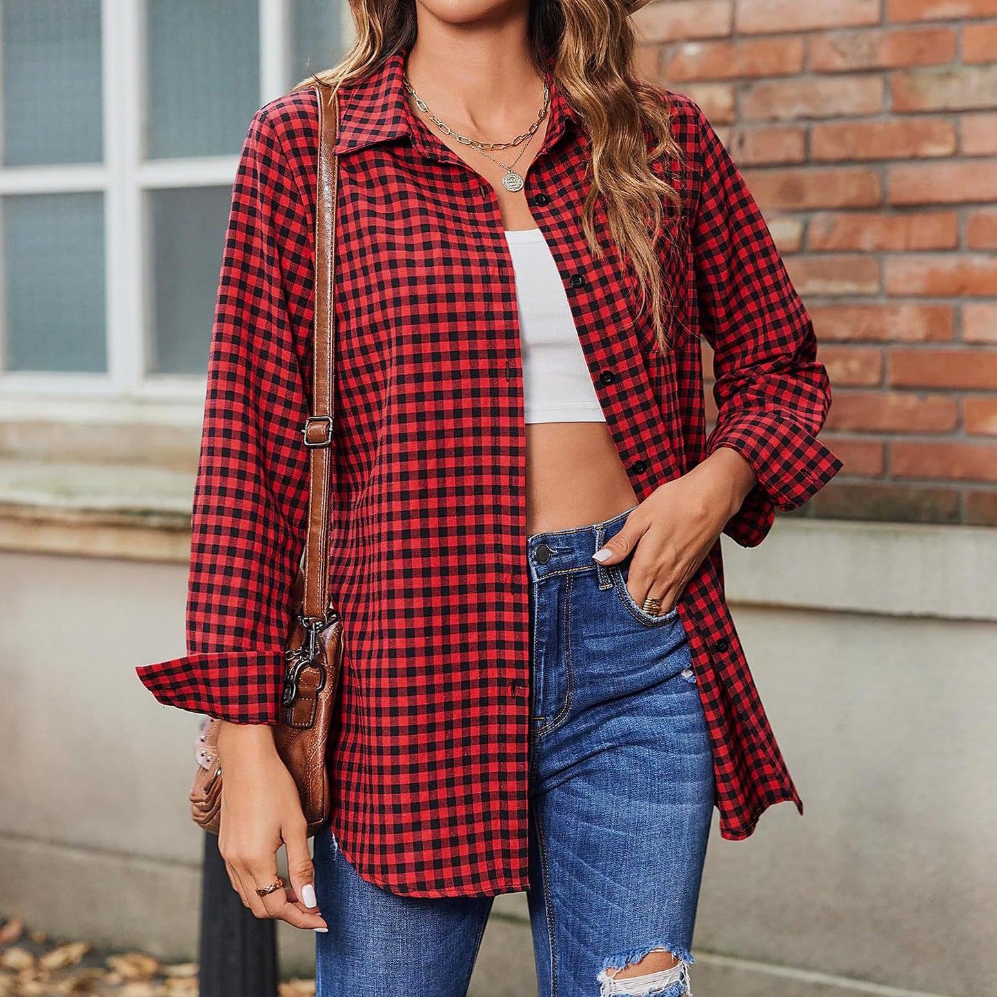 Frau in rotem kariertem Hemd, blauer Jeans und weißem Top vor Backsteinwand. Modetrend, lässiger Stil, Herbstmode, Streetwear-Look.