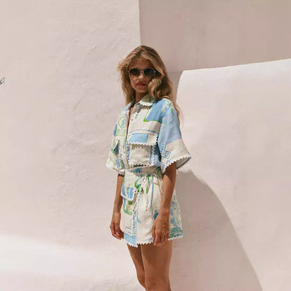 Frau in modischem Sommeroutfit mit blau-grünem Muster vor weißer Wand, trägt Sonnenbrille. Trendige Damenmode, Sommerlook, Freizeitkleidung.