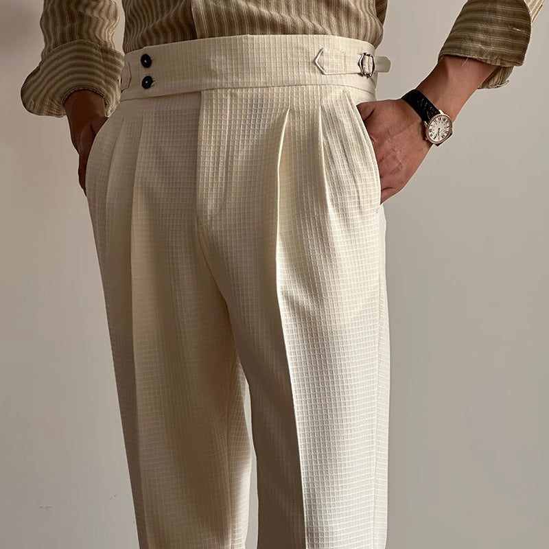 Elegante cremefarbene Anzughose mit hoher Taille und Gürtel, getragen von einer Person mit gestreiftem Hemd und Armbanduhr. Modetrend Herrenbekleidung.