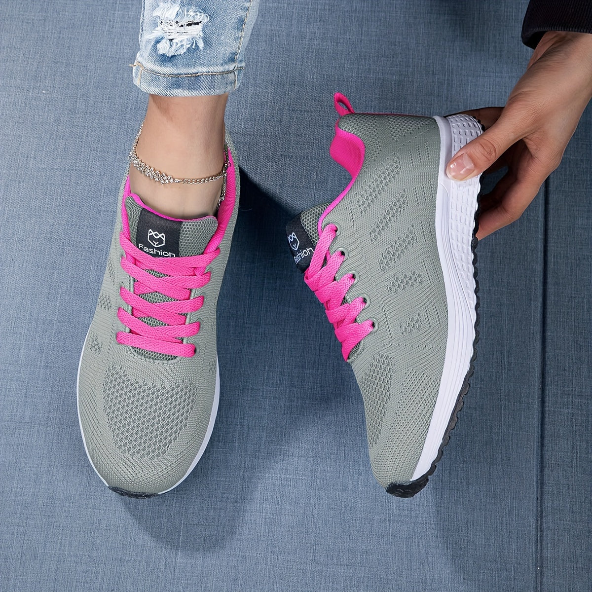 Graue Sportschuhe mit pinken Schnürsenkeln auf blauem Hintergrund, getragen von Person in Jeans. Bequeme Damen-Laufschuhe, modisch und atmungsaktiv.