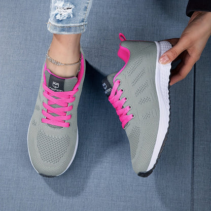 Graue Sportschuhe mit pinken Schnürsenkeln auf blauem Hintergrund, getragen von Person in Jeans. Bequeme Damen-Laufschuhe, modisch und atmungsaktiv.