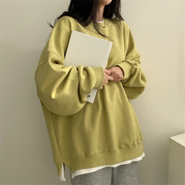 Frau in gelbem Oversize-Pullover hält weißen Laptop, lässiger Stil, moderne Mode, gemütliches Outfit, minimalistische Einrichtung.