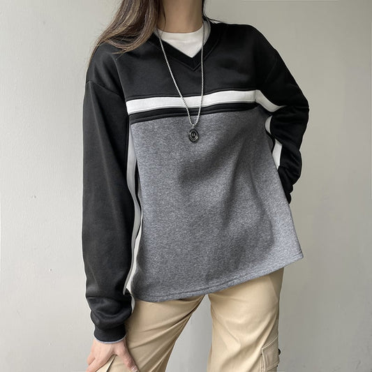Frau trägt modischen Pullover in Schwarz und Grau mit V-Ausschnitt und Kette, beige Hose. Trendige Damenmode, lässiger Stil.