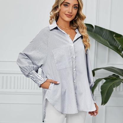 Blonde Frau in gestreifter Bluse, lächelt, steht vor weißer Wand mit Pflanze. Modetrend, Damenmode, elegante Freizeitkleidung, stilvoll.