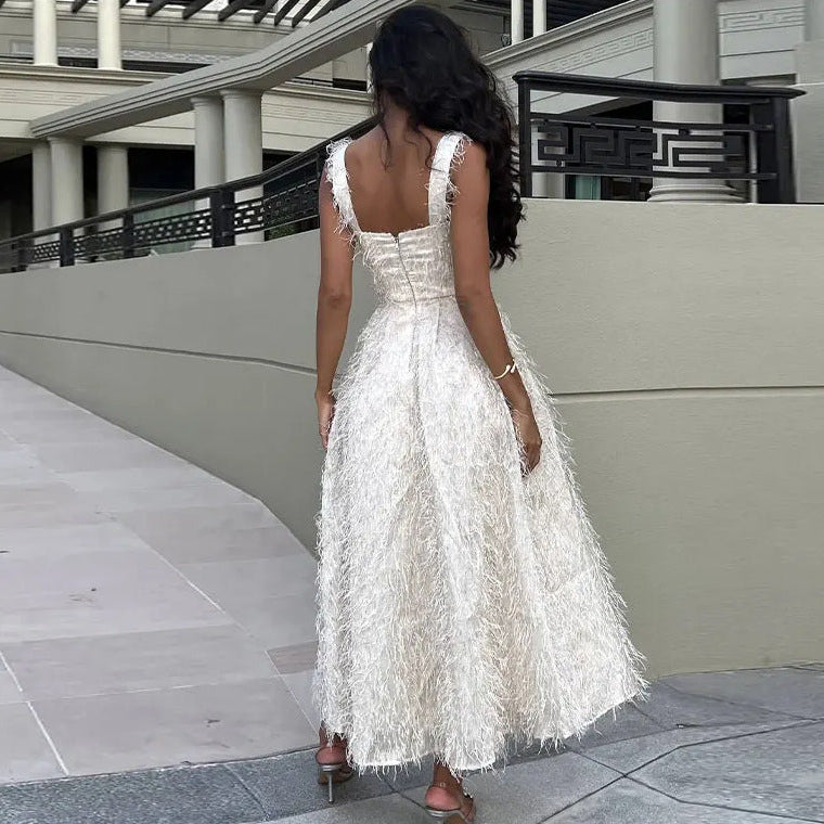 Frau in elegantem, weißem Abendkleid mit Federn, steht auf Gehweg vor moderner Architektur. Luxuriöse Mode, Abendgarderobe, stilvoller Look.