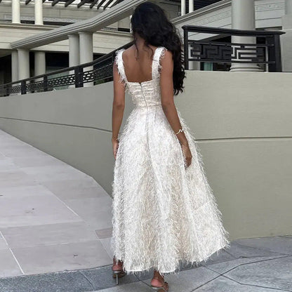 Frau in elegantem, weißem Abendkleid mit Federn, steht auf Gehweg vor moderner Architektur. Luxuriöse Mode, Abendgarderobe, stilvoller Look.