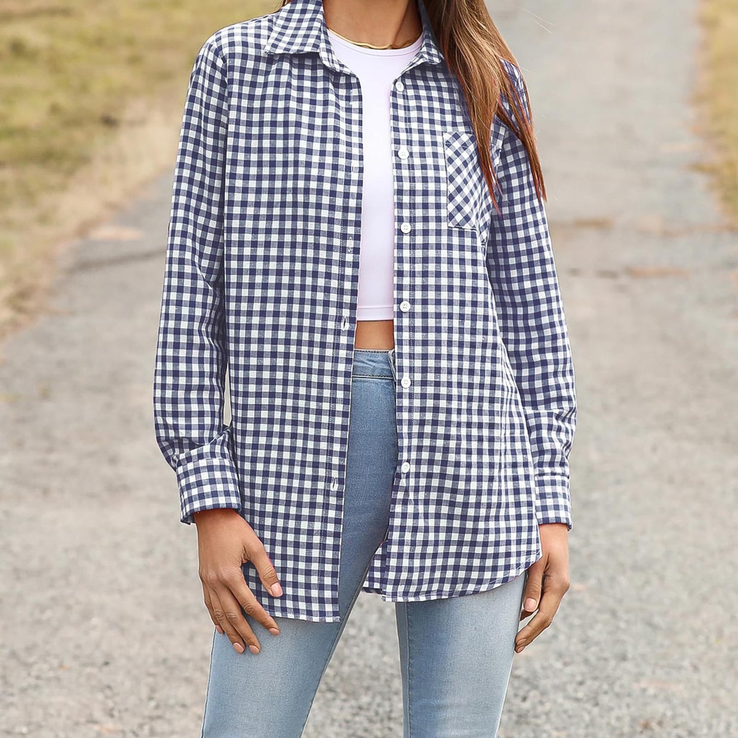 Frau in kariertem Hemd, weißem Top und blauer Jeans auf ländlichem Weg. Modetrend, Freizeitlook, Damenmode, kariertes Hemd, Outdoor-Stil.