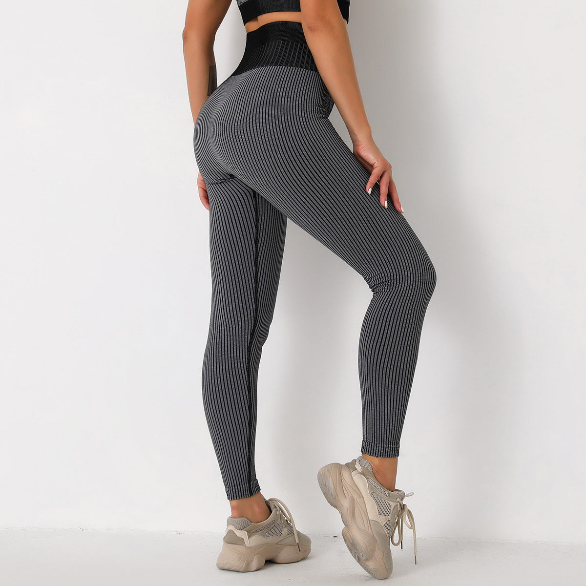 Frau in grauer, gerippter Leggings und beigen Sneakers vor weißem Hintergrund. Sportmode, Fitnessbekleidung, bequeme Leggings.