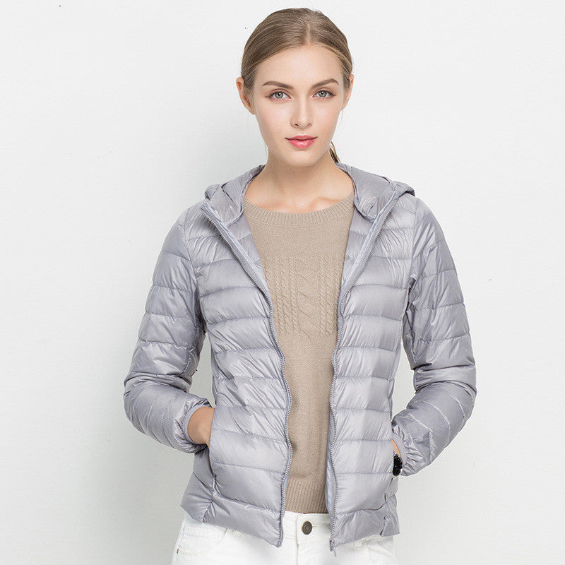 Frau in grauer Daunenjacke mit Kapuze, beige Pullover, weiße Hose. Modetrend, Winterjacke, Damenbekleidung, stilvoll, warm.