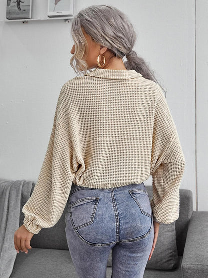 Frau mit grauem Haar trägt beige Strickpullover und blaue Jeans, steht in modernem Wohnzimmer. Modetrend, lässiger Stil, Herbstmode.