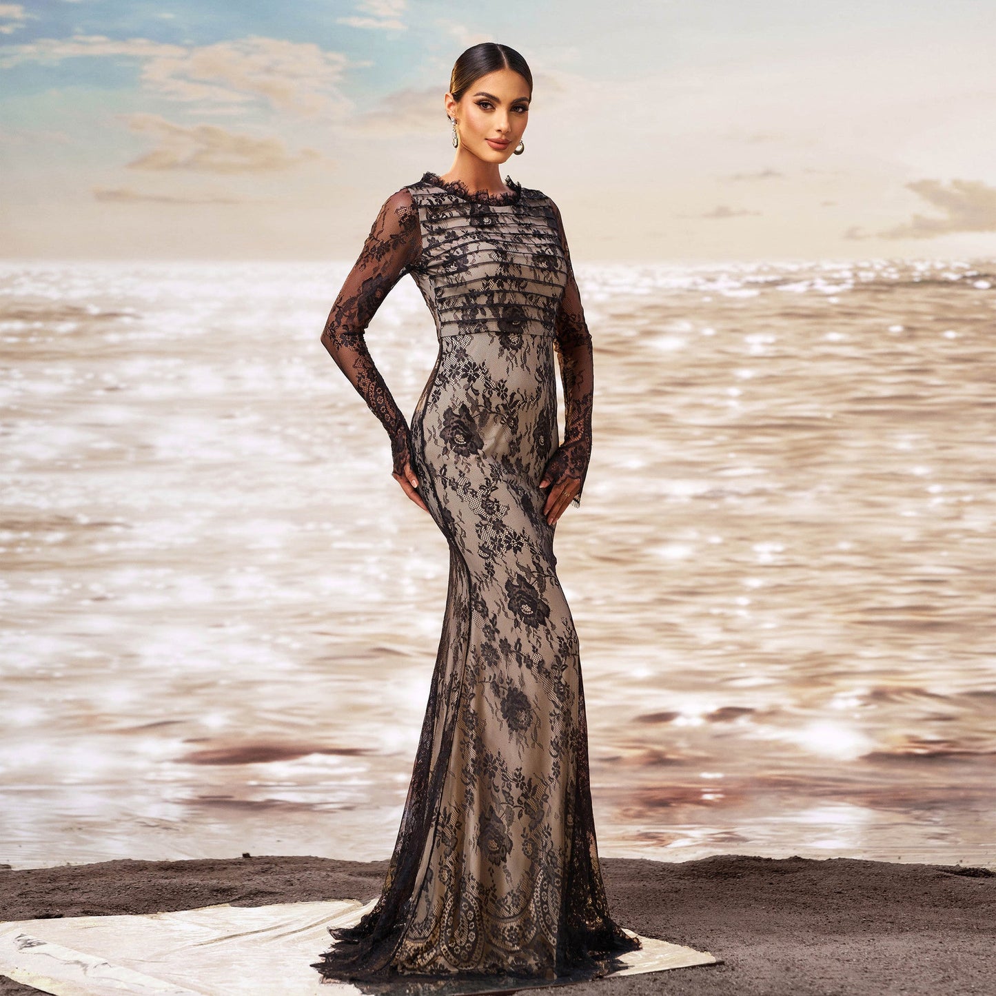 Elegantes Abendkleid mit schwarzer Spitze und floralen Mustern, getragen von einer Frau am Strand bei Sonnenuntergang. Luxuriöse Mode, Abendgarderobe.