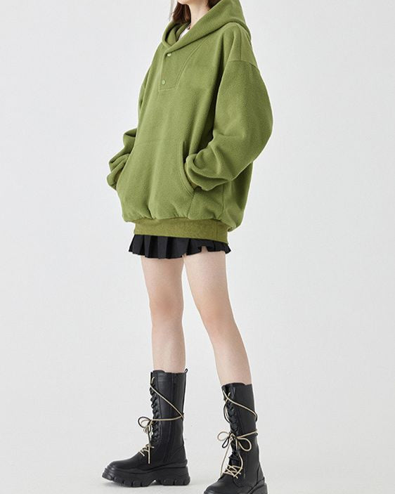 Frau in grünem Oversize-Hoodie, schwarzem Minirock und schwarzen Stiefeln. Modetrend, lässiger Stil, Herbstmode, Streetwear-Look.