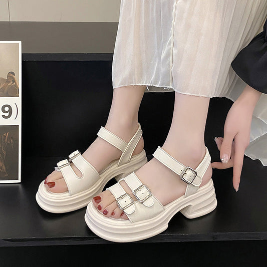 Weiße Plateau-Sandalen mit doppelten Schnallen an Frauenfüßen, kombiniert mit einem weißen Plissee-Rock. Modische Sommerschuhe für Damen.