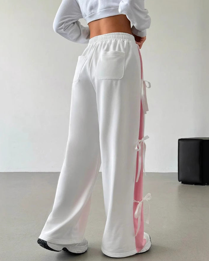 Frau in weißer Jogginghose mit rosa Streifen und Schleifen, sportlich, modern, Freizeitmode, Rückansicht, minimalistisch, Indoor.