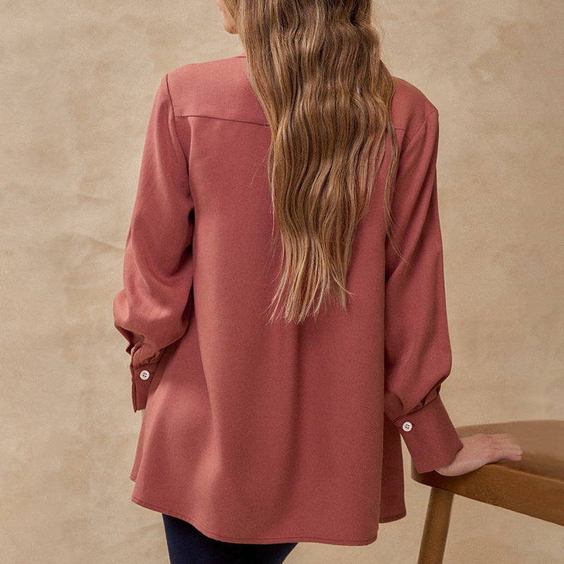 Frau mit langen, welligen Haaren trägt eine rostrote Bluse mit Knöpfen, steht vor beigem Hintergrund. Modetrend, Damenbluse, Herbstmode.