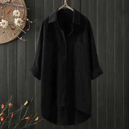 Schwarzes Leinenhemd, langärmelig, hängend vor dunklem Holzhintergrund, mit Blumenverzierung. Elegantes, minimalistisches Design für Herrenmode.