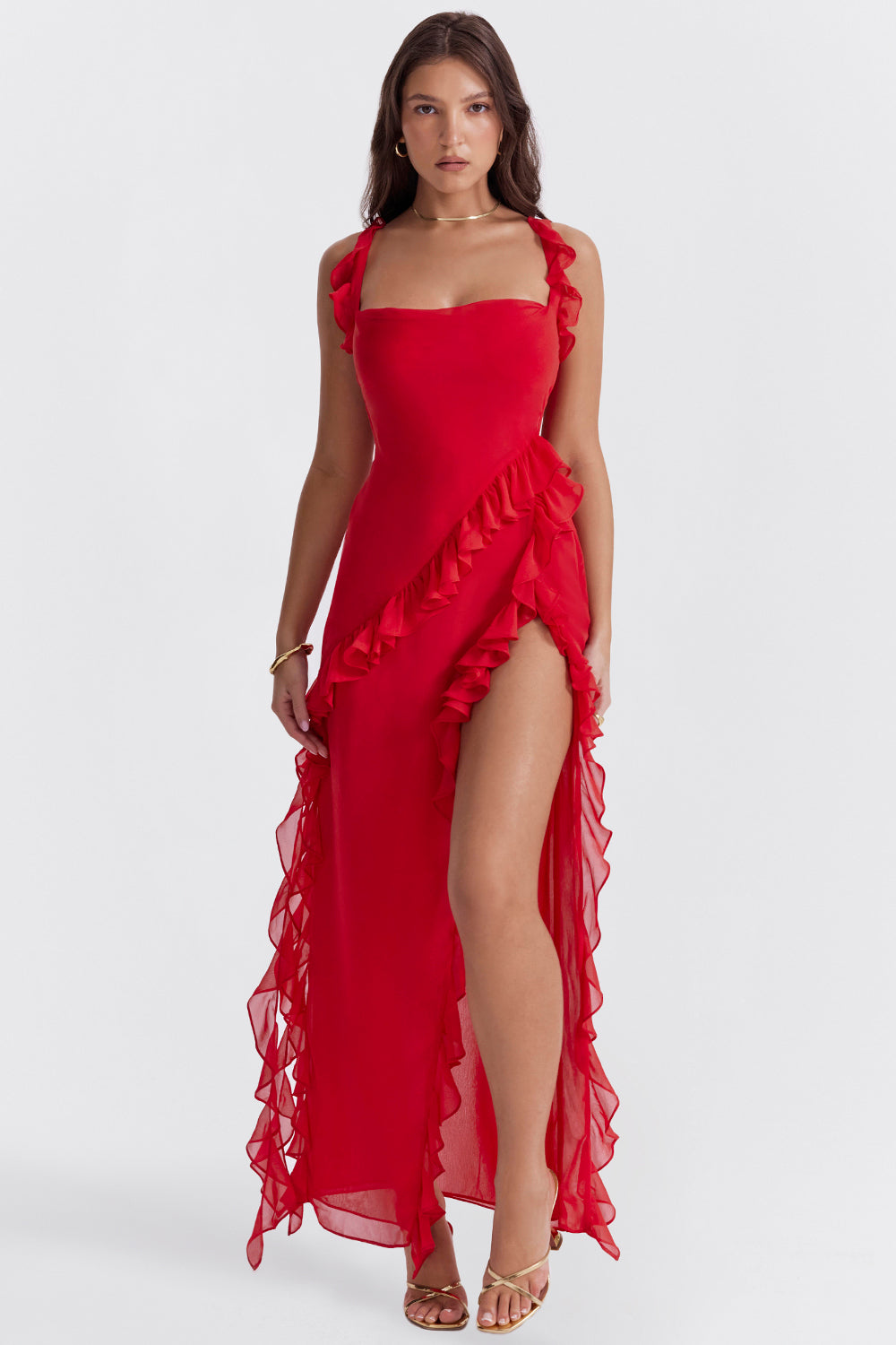 Frau in elegantem, rotem Abendkleid mit Rüschen und hohem Beinschlitz, trägt goldene Sandalen. Perfekt für formelle Anlässe und Mode-Events.