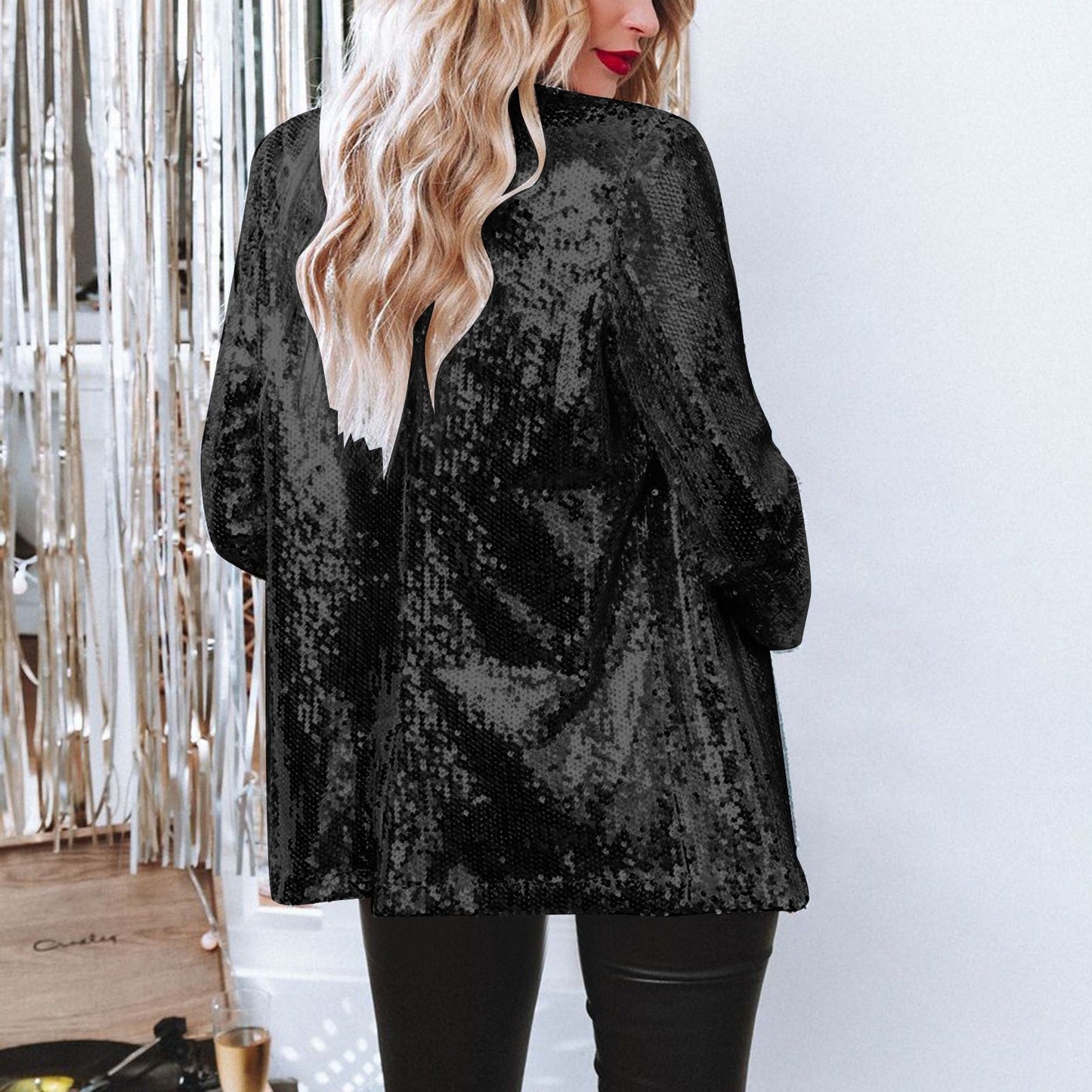 Frau in schwarzer Paillettenjacke, blondes Haar, steht vor silbernem Vorhang. Modetrend, glamouröser Look, Abendmode, stilvolle Kleidung.