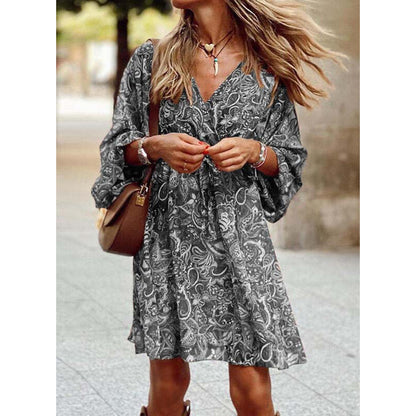 Frau in geblümtem Sommerkleid, braune Umhängetasche, modische Accessoires, lässiger Look, Stadtbummel, windgeblasene Haare, stilvoller Auftritt.