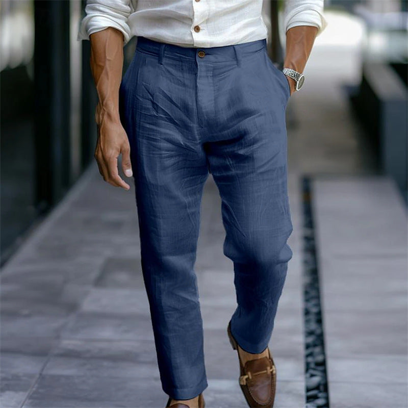 Mann in blauer Leinenhose und weißem Hemd, gehend auf einem Gehweg. Elegante Herrenmode, Sommeroutfit, braune Lederschuhe, stilvoll gekleidet.