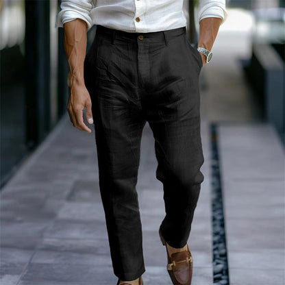 Eleganter Mann in schwarzer Leinenhose und weißem Hemd, gehend auf modernem Gehweg. Stilvolle Herrenschuhe, Armbanduhr, urbane Mode.