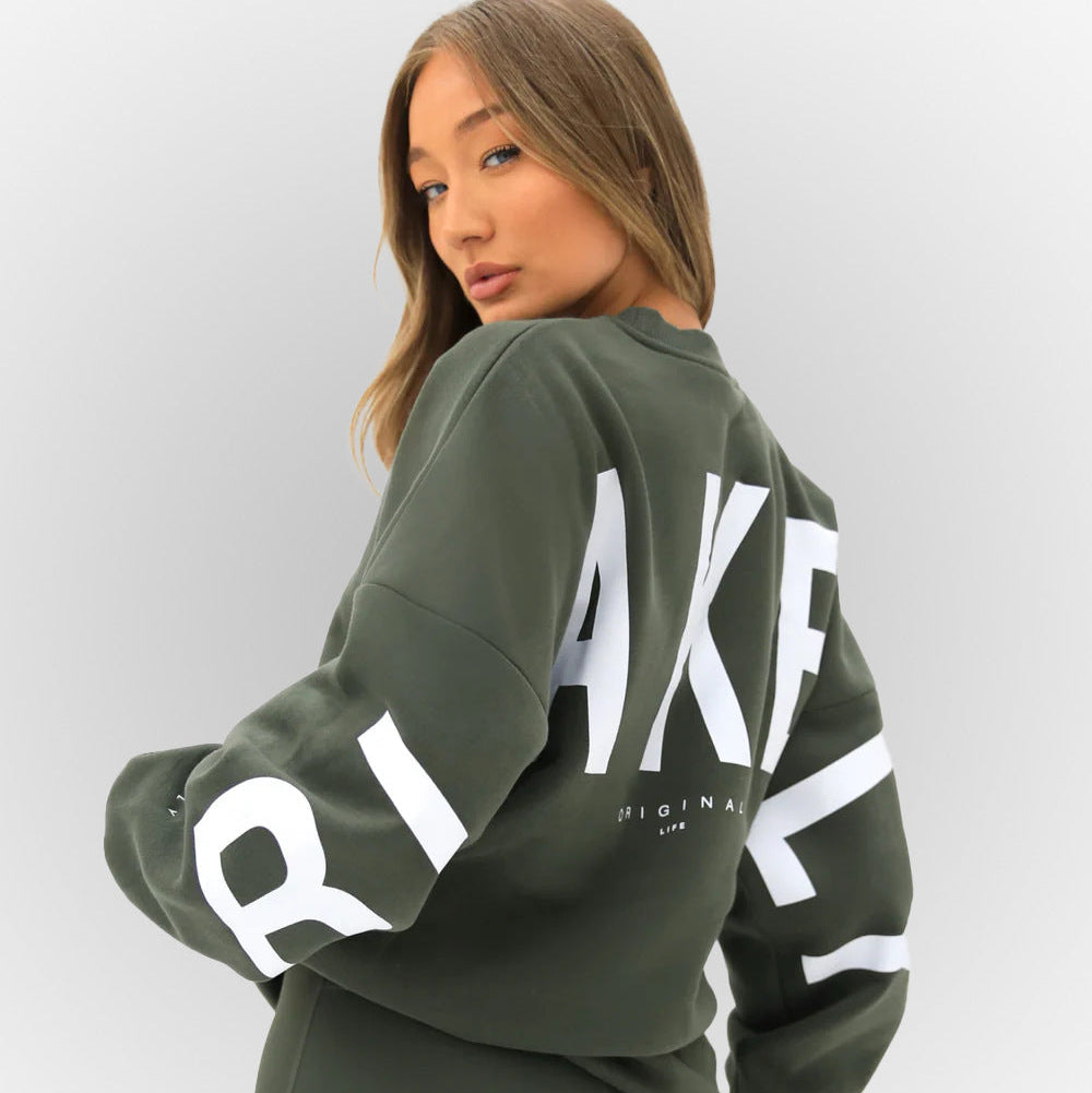 Junge Frau in olivgrünem Sweatshirt mit großem weißen Schriftzug auf Rücken und Ärmeln, modisch und lässig, Streetwear, Rückansicht.