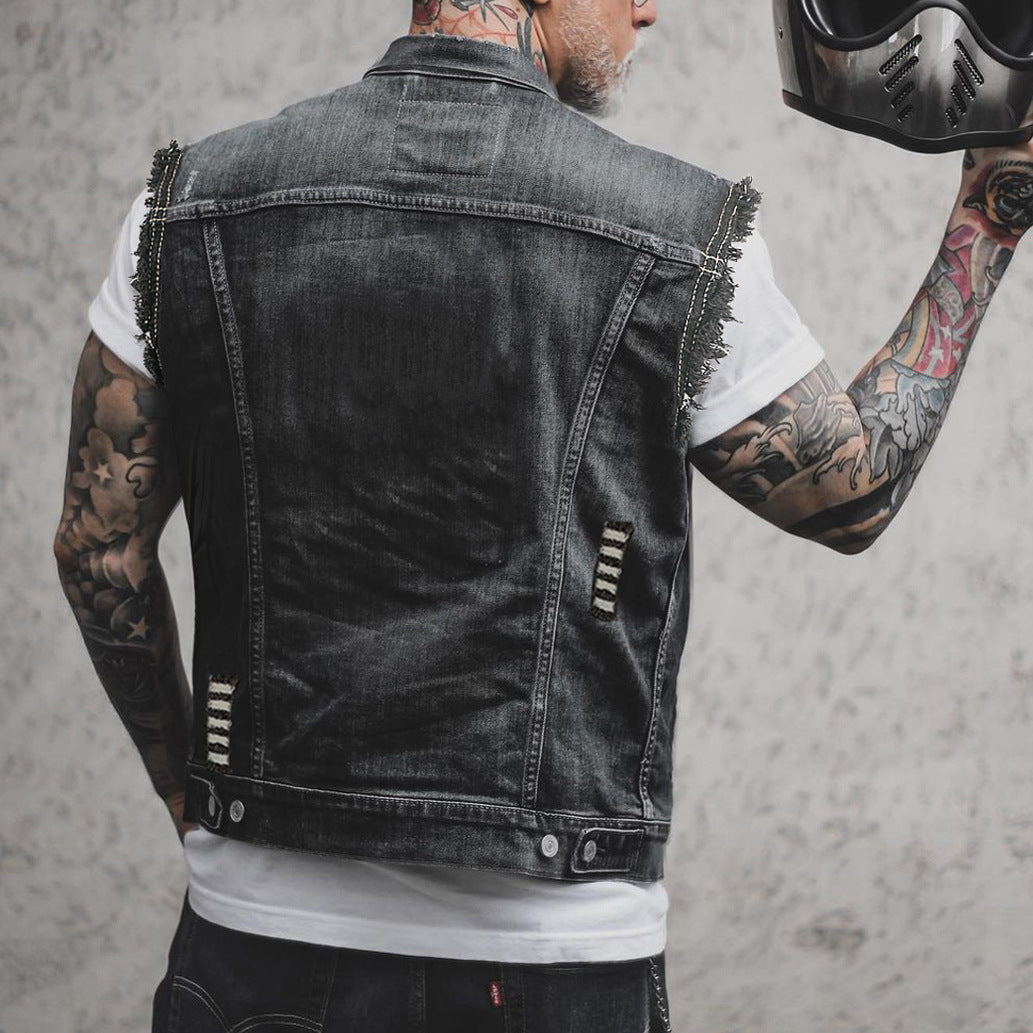 Mann mit tätowierten Armen trägt schwarze Jeansweste und hält Motorradhelm. Rocker-Stil, modische Biker-Kleidung, urbaner Look.