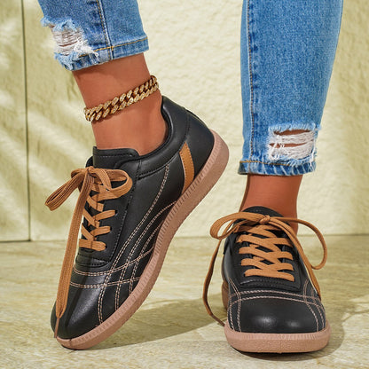 Damen Sneaker in Schwarz mit braunen Schnürsenkeln, kombiniert mit zerrissenen Jeans und goldener Fußkette. Modische Freizeitschuhe für den Alltag.
