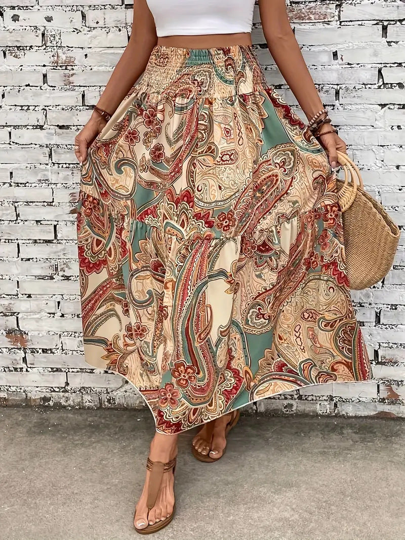 Frau in langem, geblümtem Boho-Rock vor weißer Backsteinwand, trägt Sandalen und Strohtasche. Sommermode, Boho-Chic, Damenbekleidung.