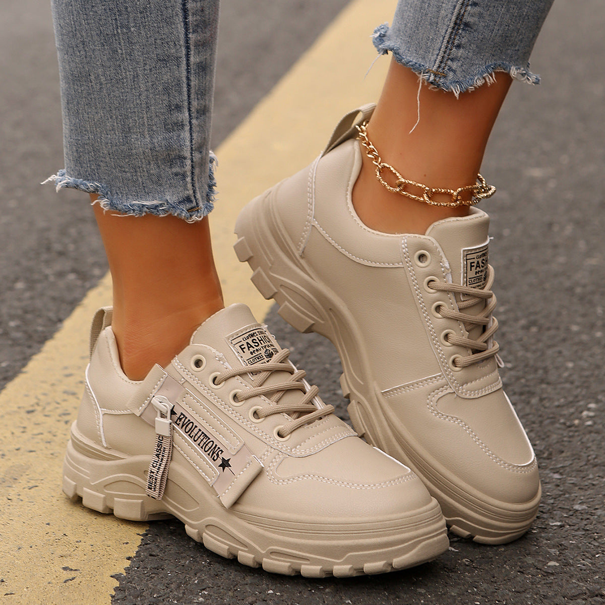 Beige Damen-Sneaker auf Asphalt, kombiniert mit zerrissenen Jeans und goldener Fußkette. Modische Straßenschuhe, ideal für urbanen Stil.