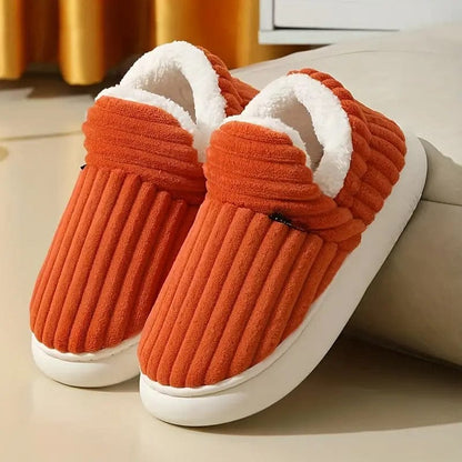 Orange Hausschuhe mit weißem Plüschfutter, gerippte Textur, auf hellem Hintergrund. Bequeme, warme Pantoffeln für den Winter.