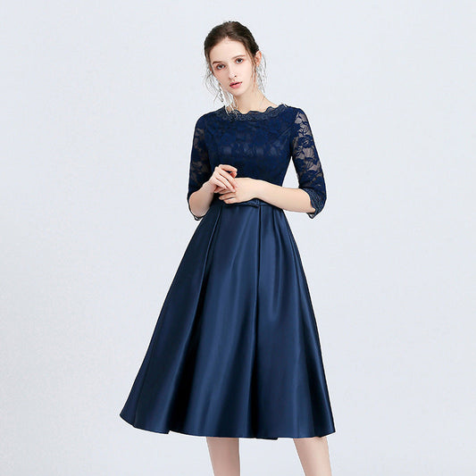 Frau in elegantem, dunkelblauem Abendkleid mit Spitzenoberteil und halblangen Ärmeln, stehend vor hellem Hintergrund.