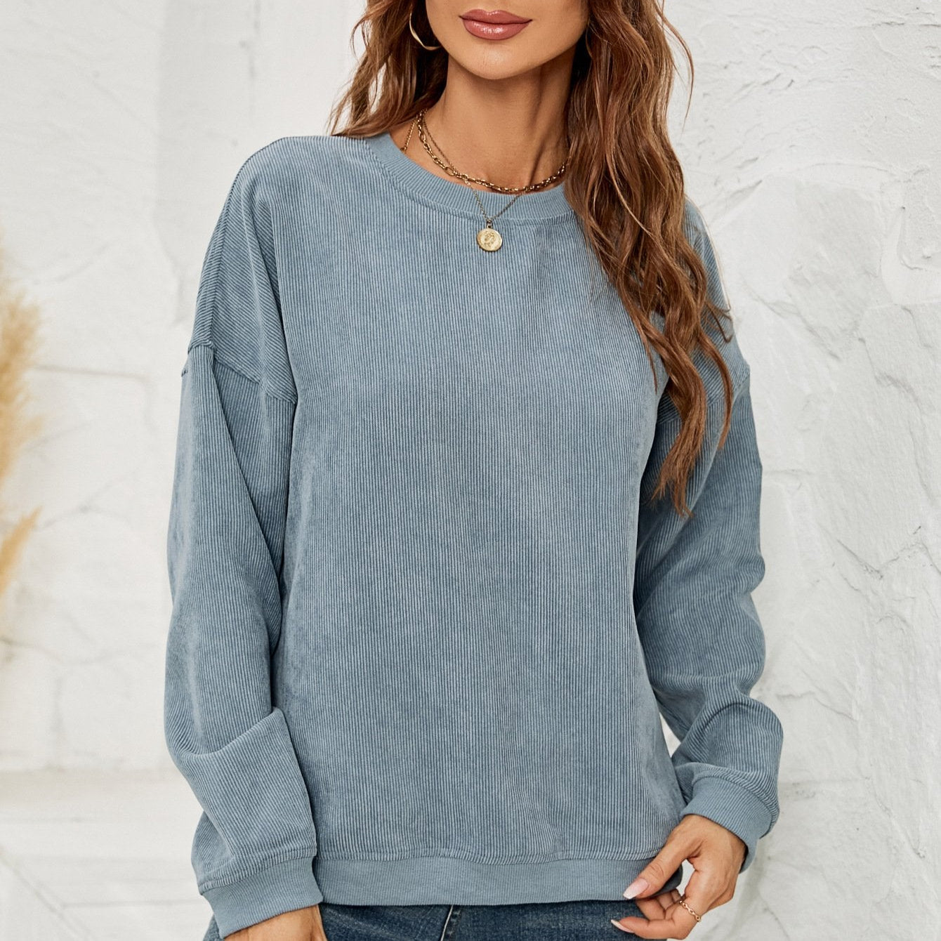 Frau in blauem Cordpullover vor weißer Wand, lässiger Herbstlook, modischer Damenpullover, gemütlicher Freizeitstil, trendige Damenmode.