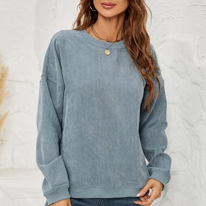 Frau in blauem Cordpullover vor weißer Wand, lässiger Herbstlook, modischer Damenpullover, gemütlicher Freizeitstil, trendige Damenmode.