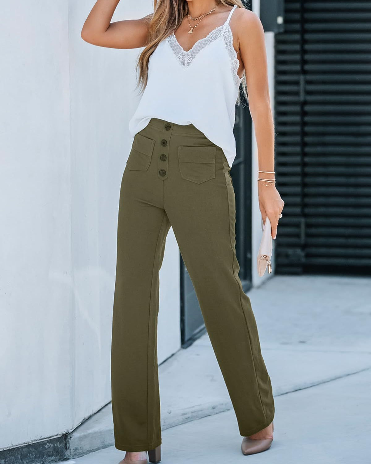 Frau in weißem Spitzen-Top und olivgrüner High-Waist-Hose mit Knöpfen, hält eine Clutch. Modetrend, elegante Damenbekleidung, Sommeroutfit.