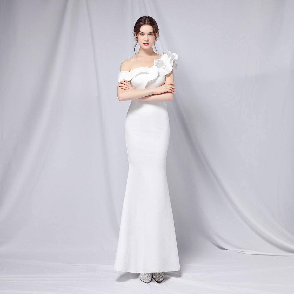 Frau in elegantem, schulterfreiem weißen Abendkleid mit Blumenapplikation, posiert vor neutralem Hintergrund. Perfekt für Hochzeiten oder Galas.