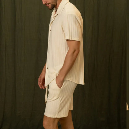 Mann in cremefarbenem, gestreiftem Kurzarmhemd und Shorts vor schwarzem Hintergrund. Sommermode, Herrenbekleidung, Freizeitlook.