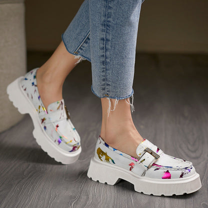 Frau trägt modische, weiße Loafer mit buntem Muster und dicker Sohle, kombiniert mit blauen Jeans. Trendige Damenschuhe, bequeme Mode.
