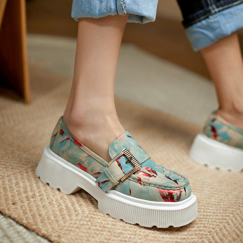 Damen-Loafer mit floralem Muster, dicker weißer Sohle und goldener Schnalle, getragen auf Teppichboden. Modische Schuhe, bequeme Damenmode.