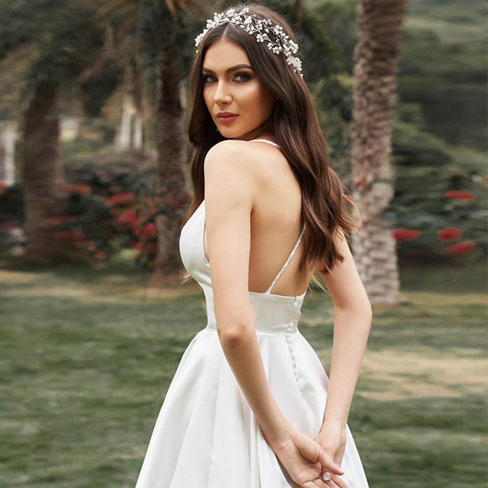 Braut in elegantem, rückenfreiem Hochzeitskleid mit Blumenhaarschmuck, steht im Garten. Perfektes Bild für Hochzeitsmode und Brautaccessoires.