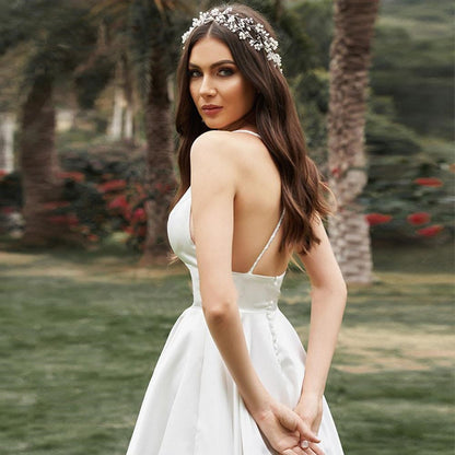 Braut in elegantem, rückenfreiem Hochzeitskleid mit Blumenhaarschmuck, steht im Garten. Perfektes Bild für Hochzeitsmode und Brautaccessoires.