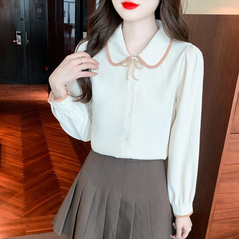 Frau in eleganter weißer Bluse mit Schleifenkragen und braunem Faltenrock, modisches Outfit, stilvolle Damenmode, Innenraum.