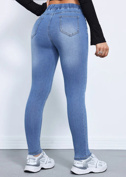 Damenjeans in hellblauem Denim, figurbetont, mit hoher Taille und Gesäßtaschen, kombiniert mit weißen Sneakers. Modische Damenbekleidung.