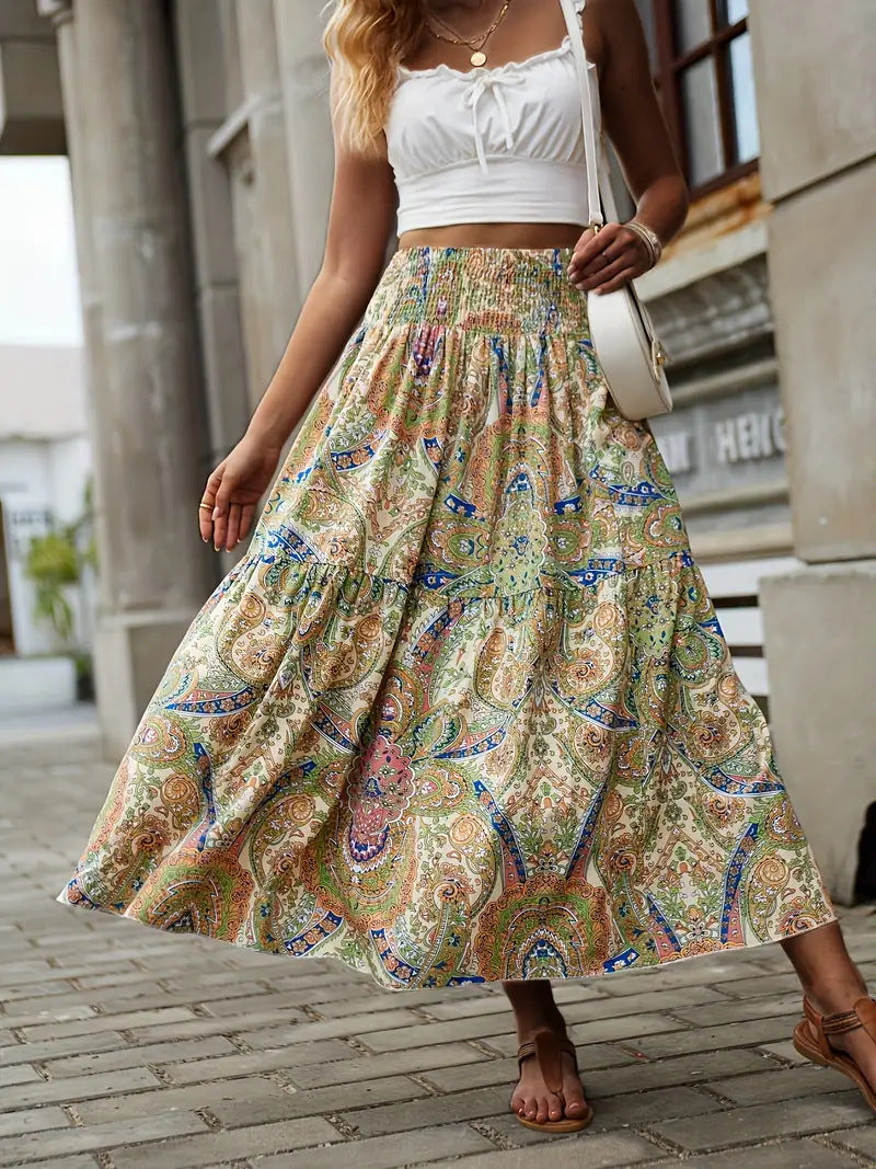 Frau in weißem Top und langem, buntem Boho-Rock mit Paisley-Muster, steht auf gepflastertem Weg. Sommermode, Streetstyle, lässiger Look.