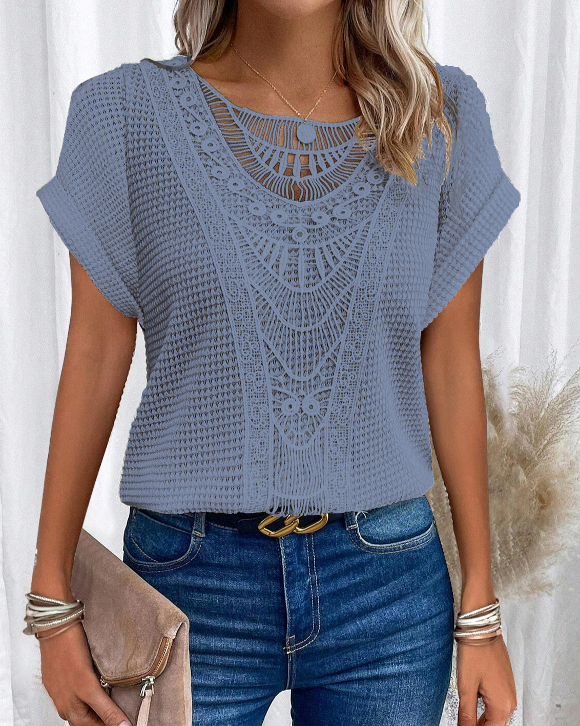 Frau trägt blaues Häkeloberteil mit Spitzenmuster, kombiniert mit blauer Jeans und Accessoires. Modetrend, Sommeroutfit, Damenmode.