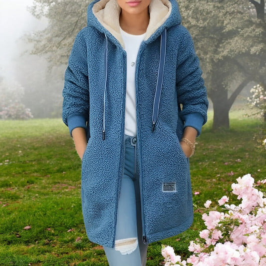 Frau in blauem Teddy-Mantel mit Kapuze im blühenden Frühlingsgarten. Modetrend, Outdoor-Bekleidung, gemütlicher Stil, Frühlingsmode.