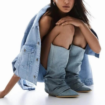 Frau in hellblauer Jeansjacke und passenden Stiefeln, sitzt auf dem Boden. Modetrend, Denim-Outfit, stilvolle Damenbekleidung.