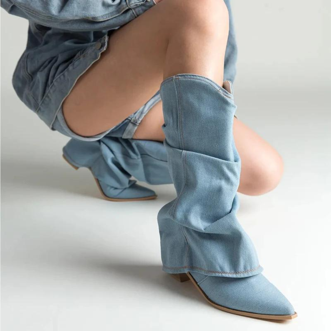 Damen in hellblauen Denim-Stiefeln und passendem Rock, kniend auf hellem Hintergrund. Modetrend, Jeansstiefel, Streetstyle.